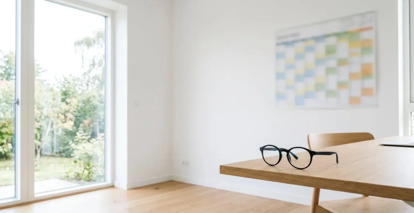 Vue large d'un bureau moderne avec calendrier mural, lunettes posées et lumière naturelle